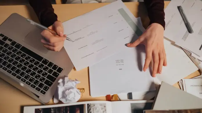 como-testar-ferramenta-ia-rotina-checklist Pessoa revisando anotações e documentos ao lado de um notebook